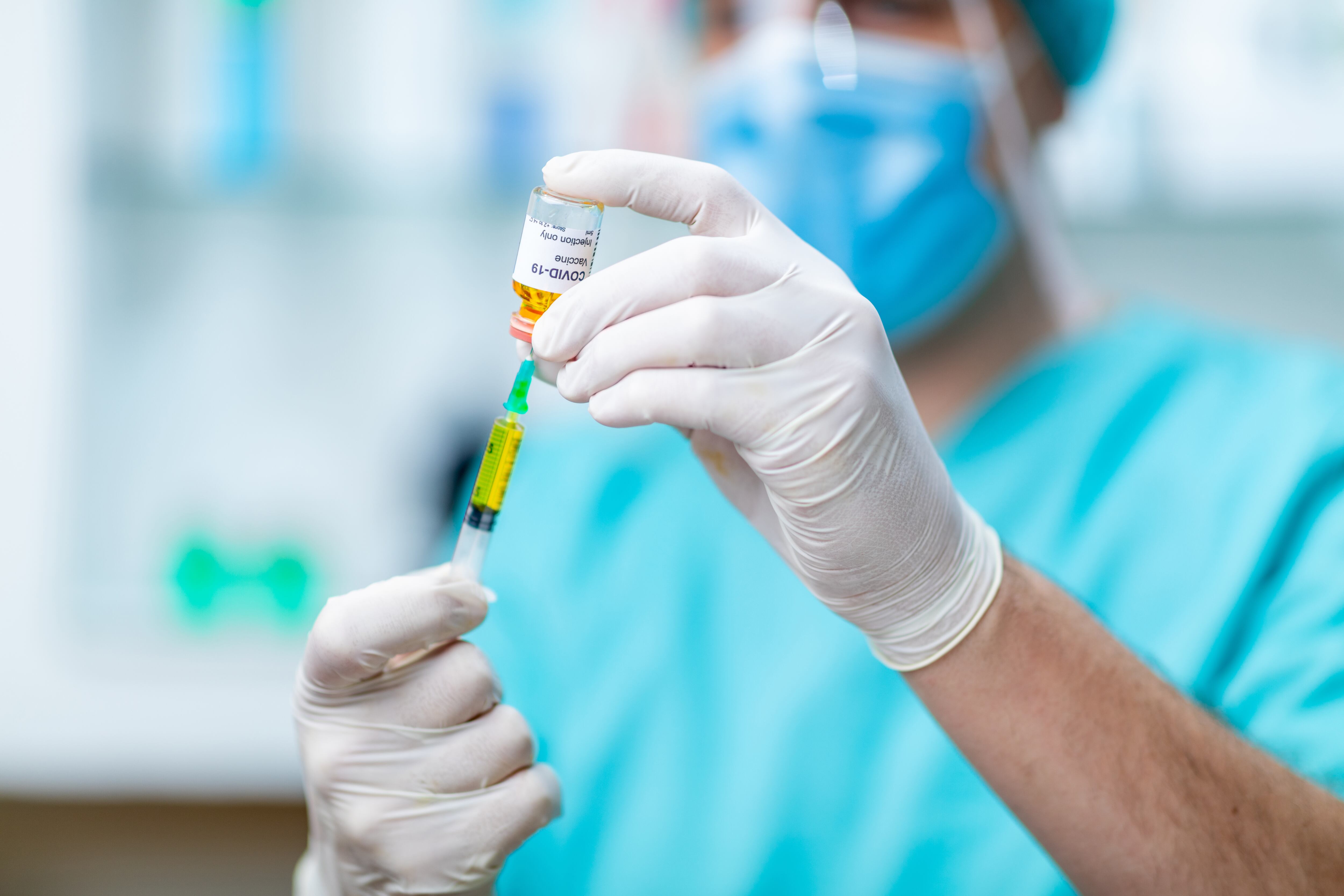 Doctor's hands in protective gloves holding COVID-19 vaccine vial and using syringe to pull liquid out
