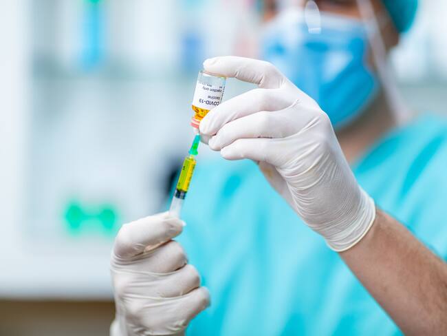 Doctor's hands in protective gloves holding COVID-19 vaccine vial and using syringe to pull liquid out