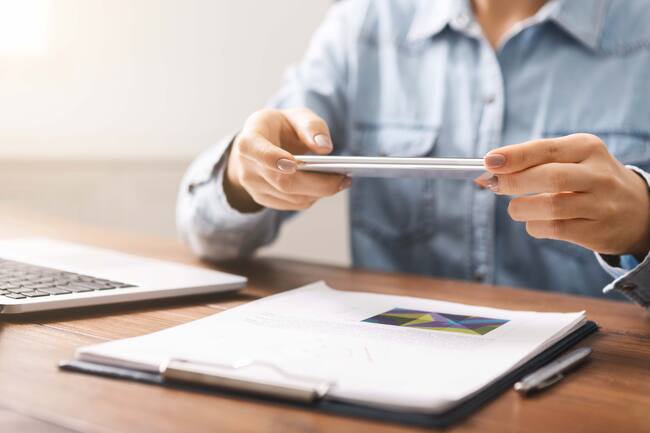 Mujer tomándole foto a un documento con su celular (Getty Images)