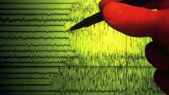 A seismographer uses a pen to point out the initial shock waves of an earthquake charted on a seismograph.