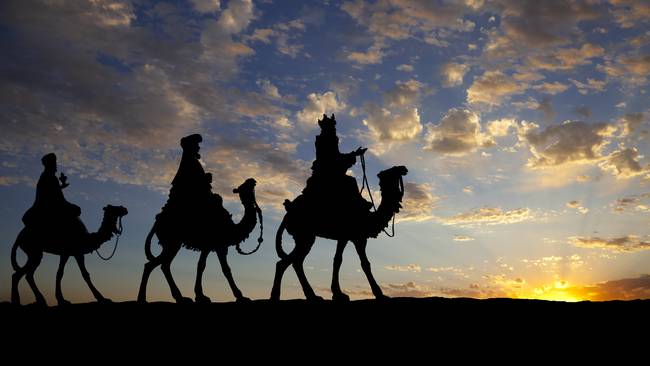Los tres reyes en camellos contra un sol poniente.
